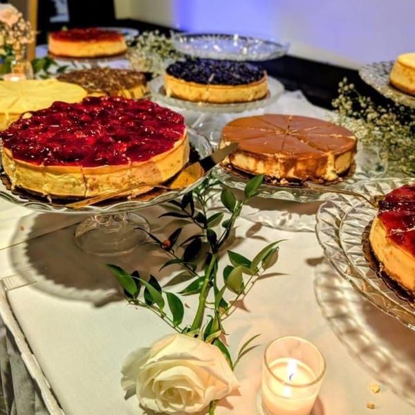 A dessert table with various cheesecakes, including strawberry, blueberry, and caramel, with floral decorations.