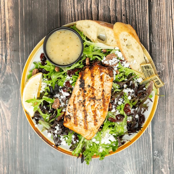 Grilled salmon salad with mixed greens, cranberries, feta, lemon, dressing, and baguette slices.