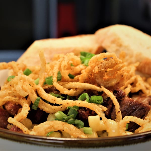 Close-up of beef and macaroni with crispy fried onions, green onions, and bread slices.