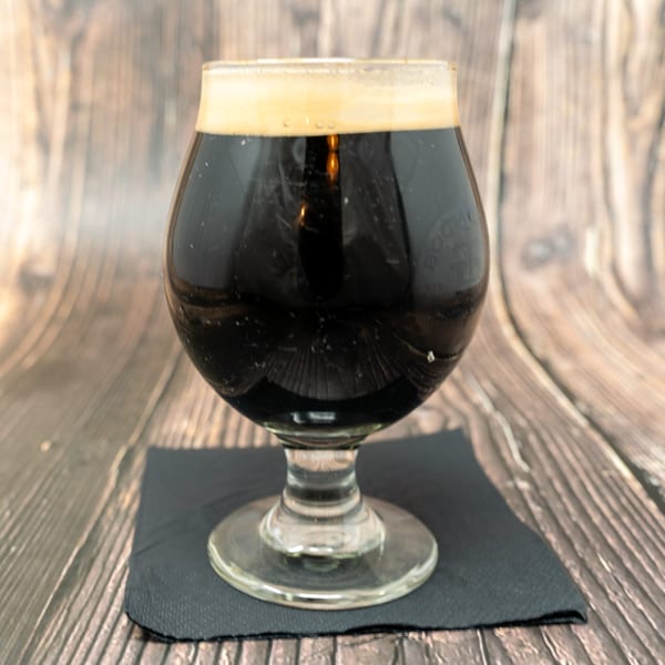 Dark beer with a frothy head in a snifter glass on a black napkin.