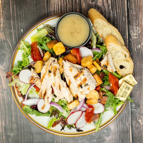 Grilled chicken salad with mixed greens, radishes, croutons, bacon, sun-dried tomatoes, and dressing.