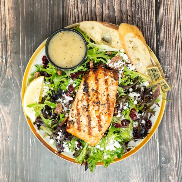 Grilled salmon salad with mixed greens, feta, cranberries, pecans, lemon, dressing, and baguette slices.