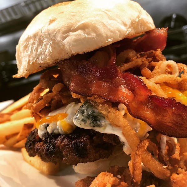 A towering burger with bacon, crispy fried onions, melted cheese, and a side of fries.