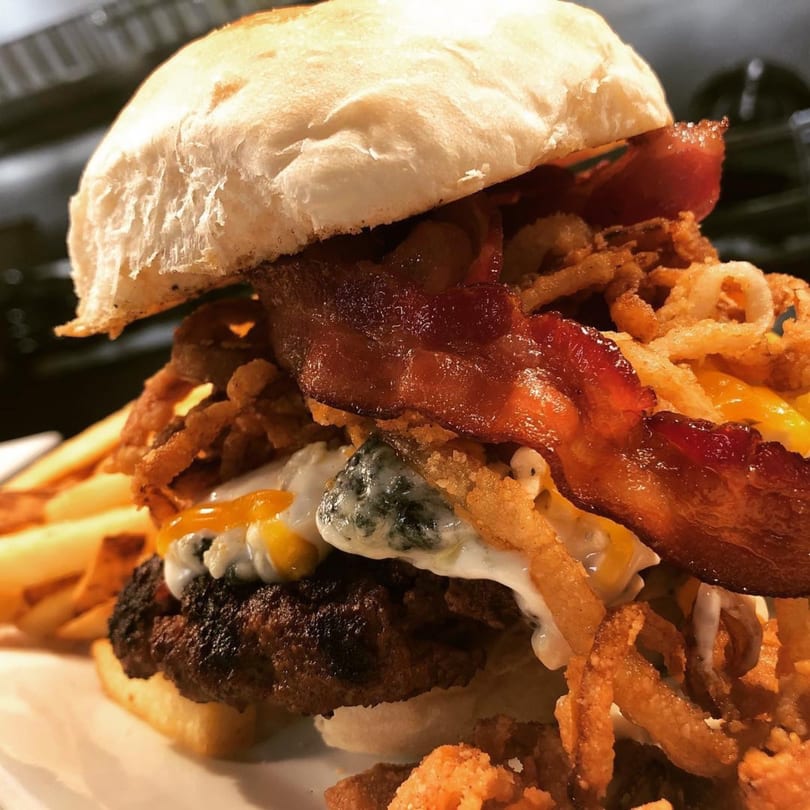 A towering burger with bacon, crispy fried onions, melted cheese, and a side of fries.