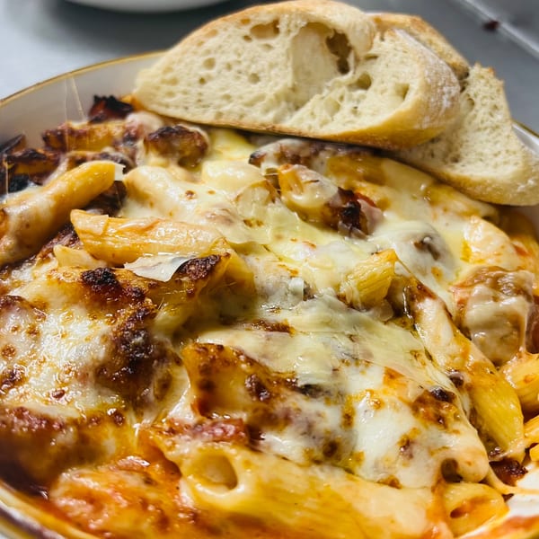 Baked penne pasta with melted cheese and tomato sauce, served with crusty bread.