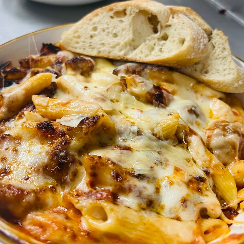 Baked penne pasta with melted cheese and tomato sauce, served with crusty bread.