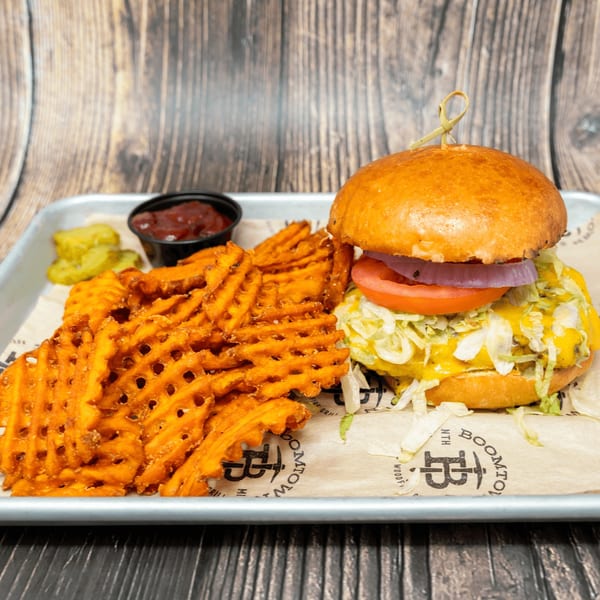 A cheeseburger with lettuce, tomato, and onion, waffle fries, pickles, and ketchup on a tray.