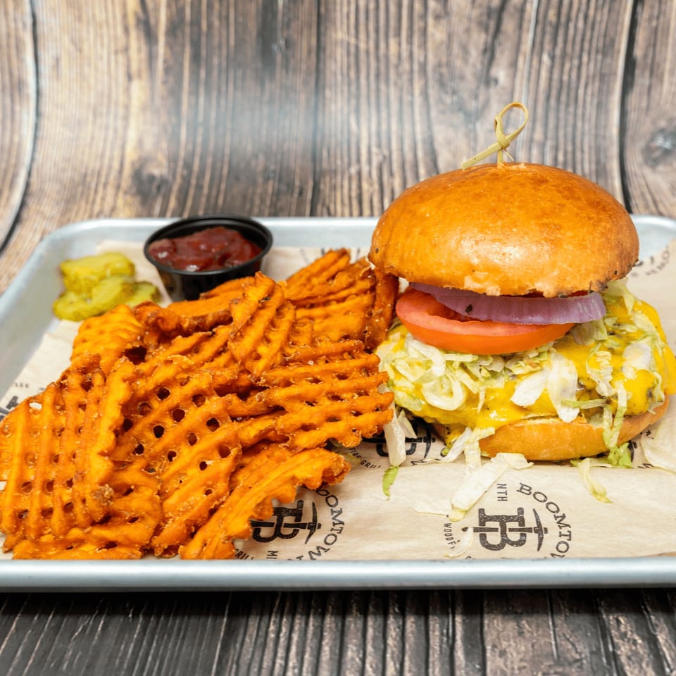 A cheeseburger with lettuce, tomato, and onion, waffle fries, pickles, and ketchup on a tray.