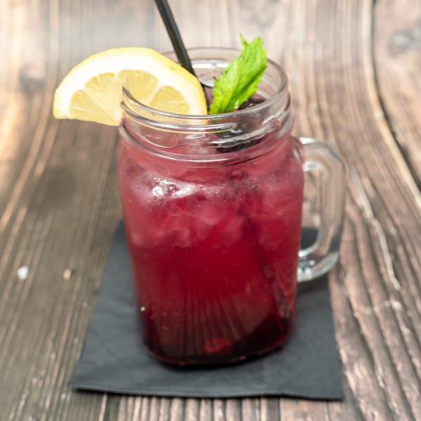A vibrant red berry cocktail in a mason jar, garnished with a lemon slice and mint.