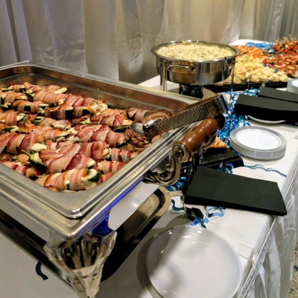 A buffet table with chafing dishes of bacon-wrapped appetizers and other food items.