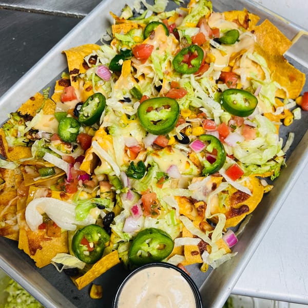 A tray of loaded nachos with cheese, lettuce, tomatoes, jalapeños, and a side of sauce.