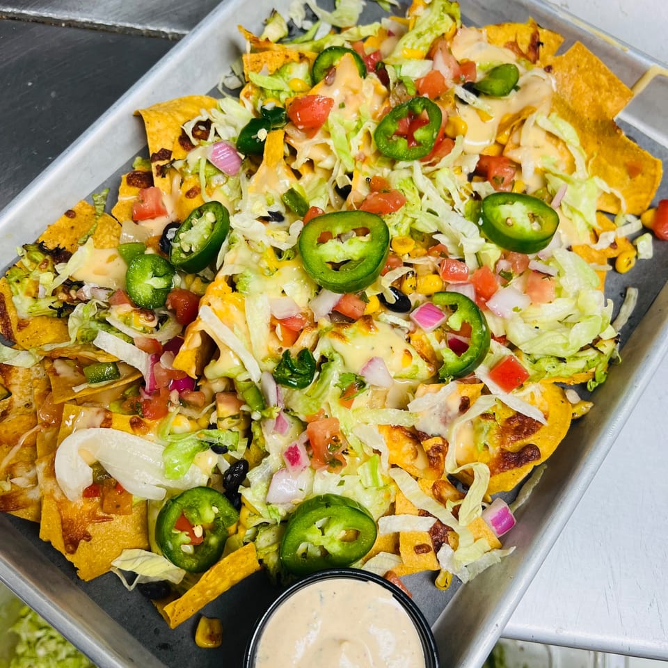 A tray of loaded nachos with cheese, lettuce, tomatoes, jalapeños, and a side of sauce.