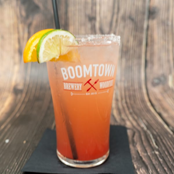 A Boomtown Brewery Woodfire cocktail, garnished with orange and lime slices, on a wooden table.