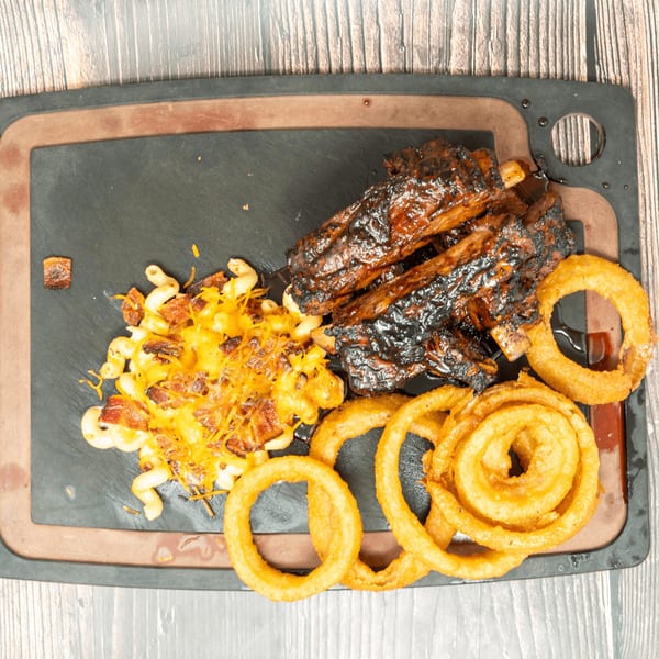 BBQ ribs, cheesy macaroni, and crispy onion rings on a dark serving board.