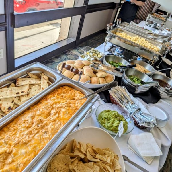 A buffet spread with various dishes including a cheesy dip, flatbread, rolls, guacamole, and mac and cheese.