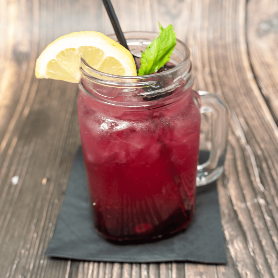 A vibrant red drink in a mason jar, garnished with a lemon slice and mint, on a wooden table.