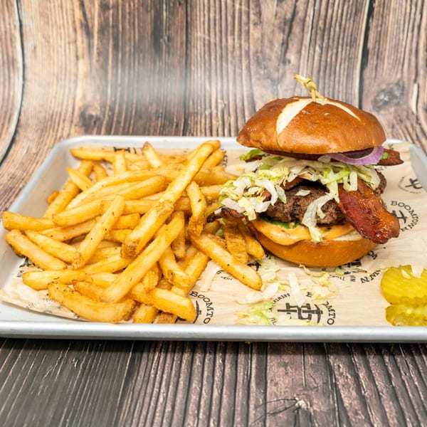 A bacon cheeseburger on a pretzel bun with fries and pickles on a metal tray.