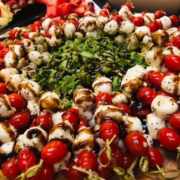 Caprese skewers with cherry tomatoes, mozzarella balls, arugula, and balsamic glaze.